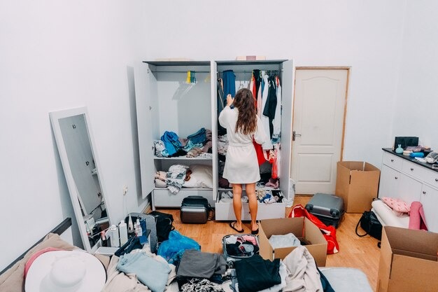 A woman stands in a room filled with various clothes, surrounded by colorful garments and accessories