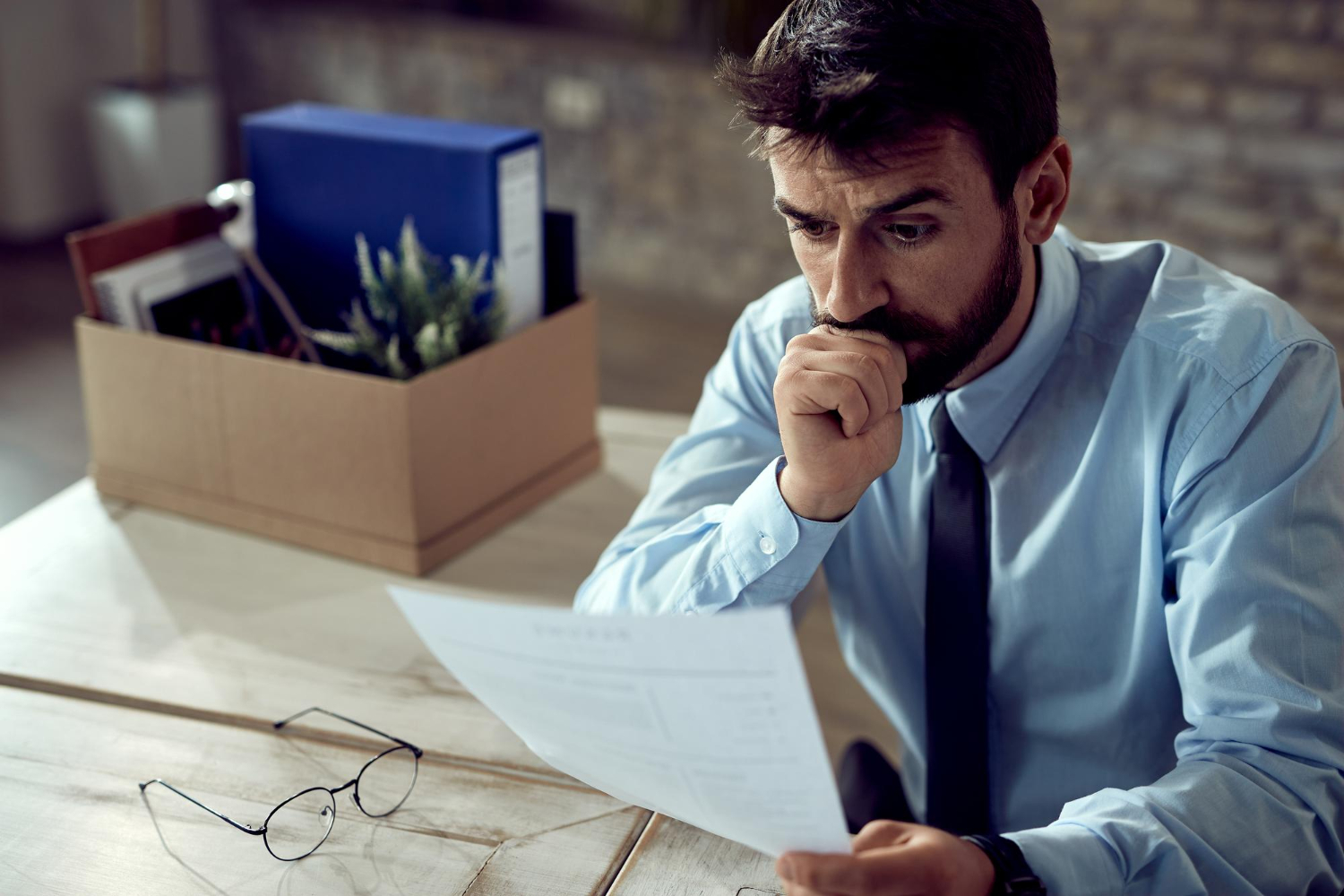 A man in a shirt and tie sits at a desk, focused on a piece of paper in front of him